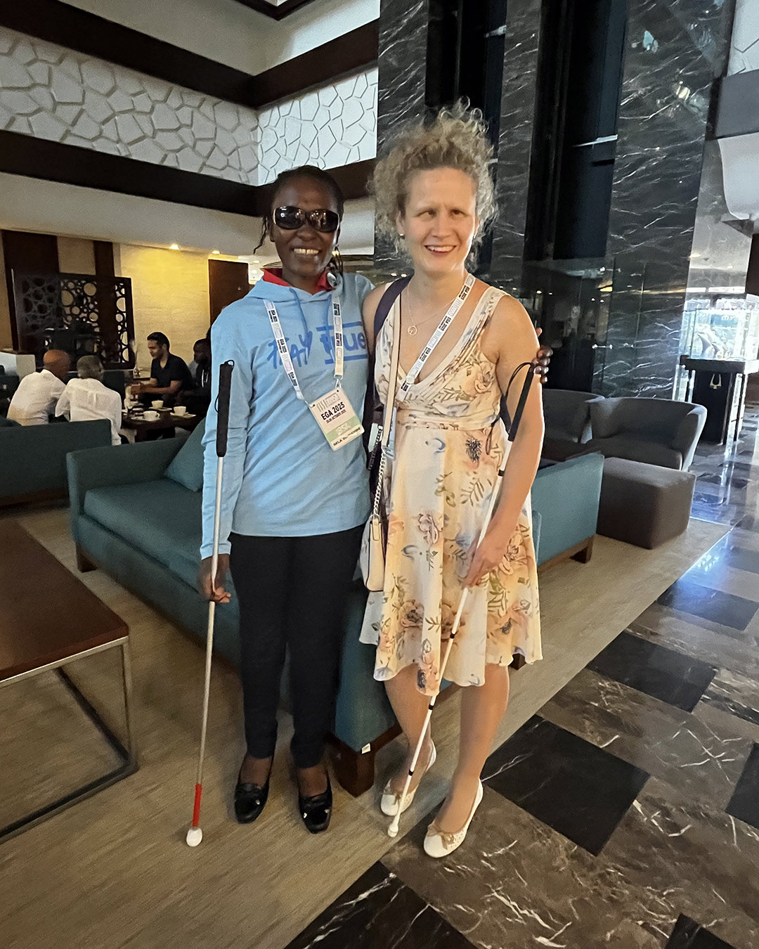 Odhiambo ja Tolppanen poseeraavat yhteiskuvassa aulatilassa, taustalla sohvapöydän ääressä istuvia ihmisiä.